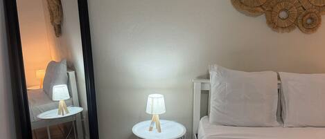 A hotel room with a bed, two bedside tables with lamps, a wall-mounted decorative item, and a large mirror.