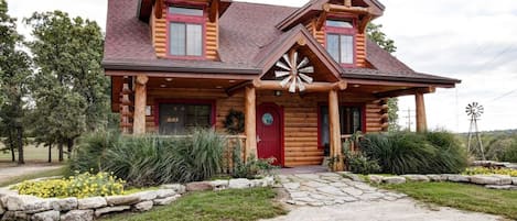 A log cabin with a red door, two chimneys, and a windmill in the background.