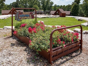 A metal bed frame with a sign that reads 'SWEET DREAMS & MOONBEAMS' in a garden setting with flowers and a wooden cabin in the background. - Branson | Family Nature Getaway | Pool + Disc Golf | 2BR (Ridgedale)