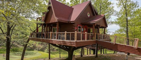 A wooden cabin with a red roof, elevated on stilts, surrounded by trees.