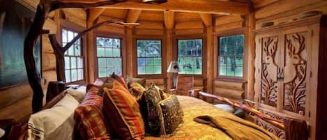 A log cabin bedroom with a large bed, multiple windows, and a wooden ceiling.