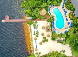 Vista aèria d'un complex turístic amb una gran piscina, gandules i un pont sobre l'aigua.