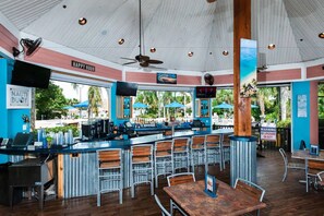 A bar area with a counter, multiple seating options, and a view of the outdoors. - Spacious Ground Floor Condo With Pool View! (Davenport)