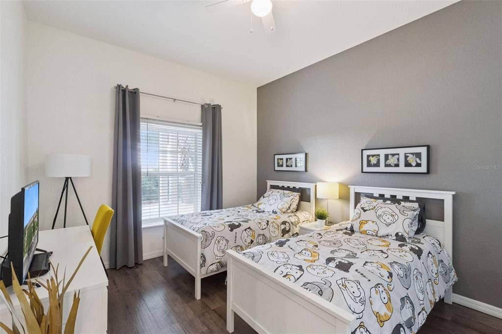 Une chambre avec deux lits, un bureau, une chaise, une lampe et une fenêtre avec des rideaux.