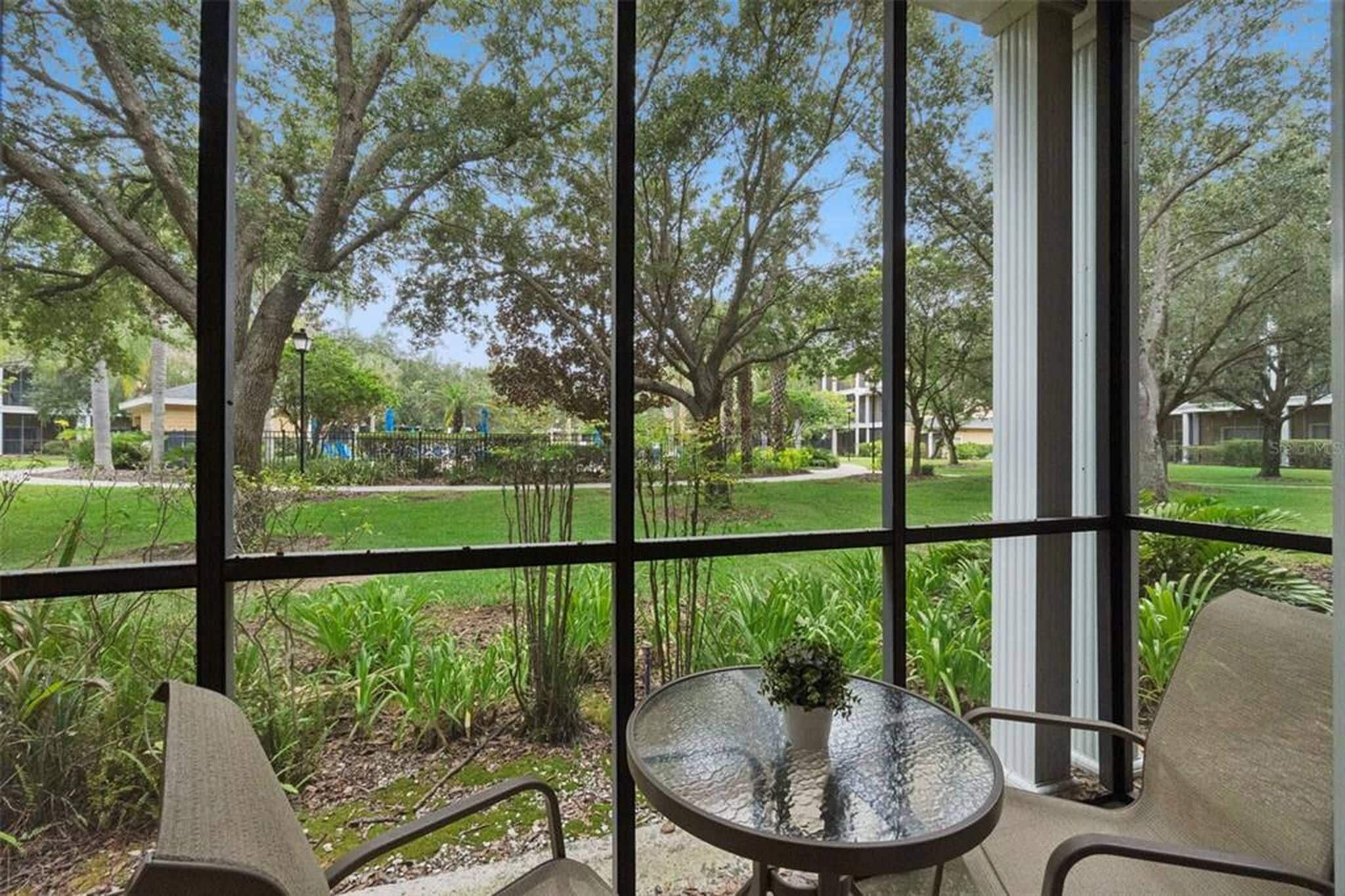 A conservatory with a glass table and chairs, overlooking a well-maintained garden and a residential area.