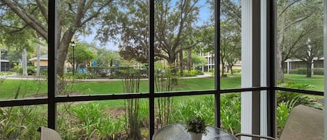 A conservatory with a glass table and chairs, overlooking a well-maintained garden and a residential area.