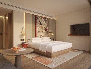 Ett modernt hotellrum med en stor säng, en tv, ett konstverk som hänger på väggen och ett litet bord med frukt.
