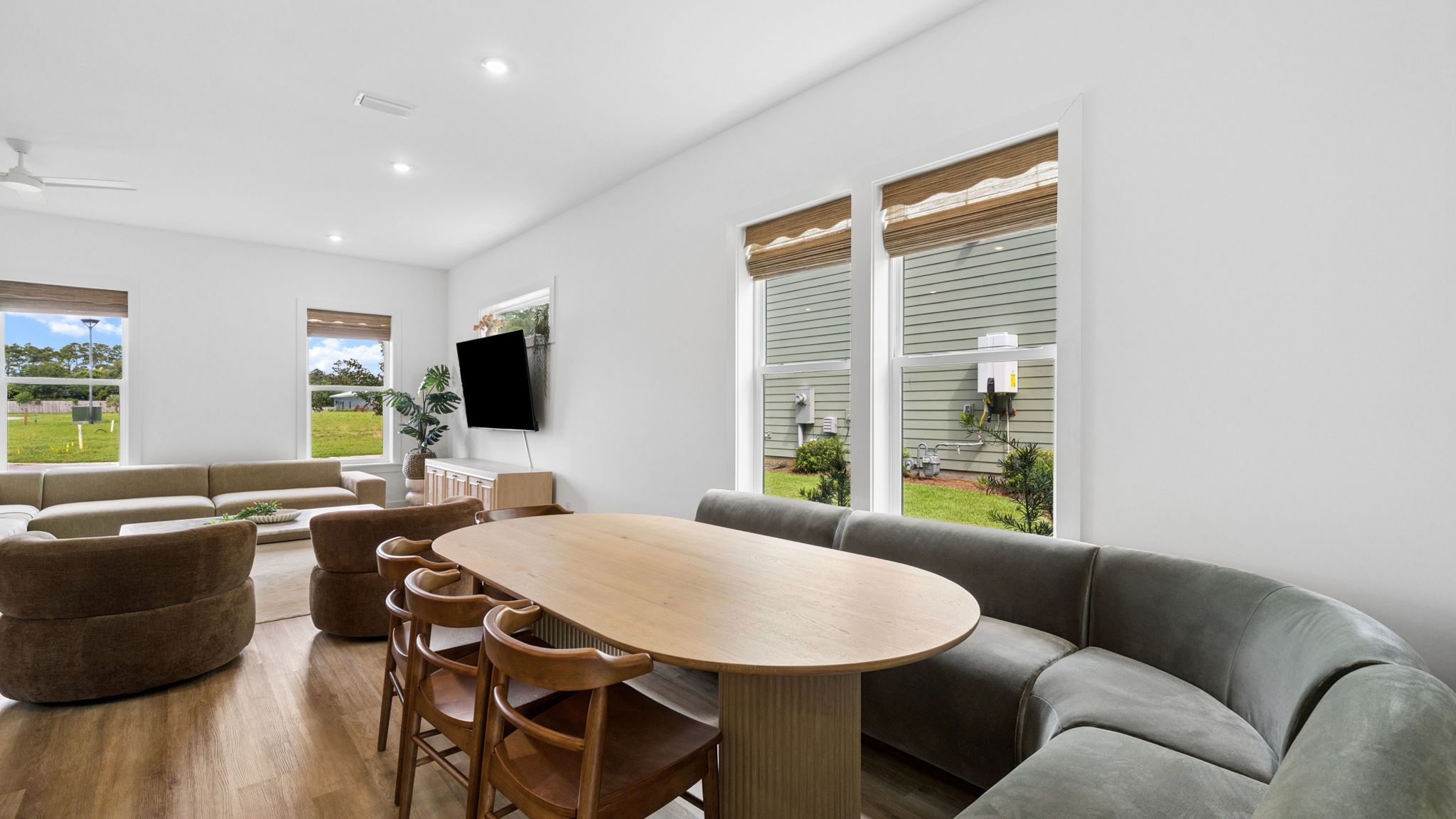 Uma sala de estar moderna com uma mesa de jantar de madeira, sofás cinzas e uma TV de tela plana na parede.