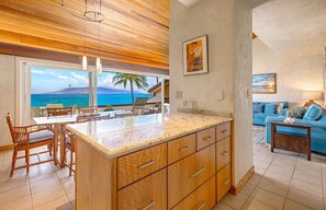 A kitchen with a large island, wooden cabinets, and a view of the ocean. - Top Floor Oceanfront 2BR on Po'olenalena Beach (Kihei)