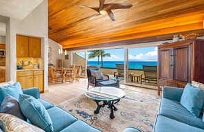 A spacious living area with a view of the ocean, a ceiling fan, and a dining area with wicker furniture. - Top Floor Oceanfront 2BR on Po'olenalena Beach (Kihei)