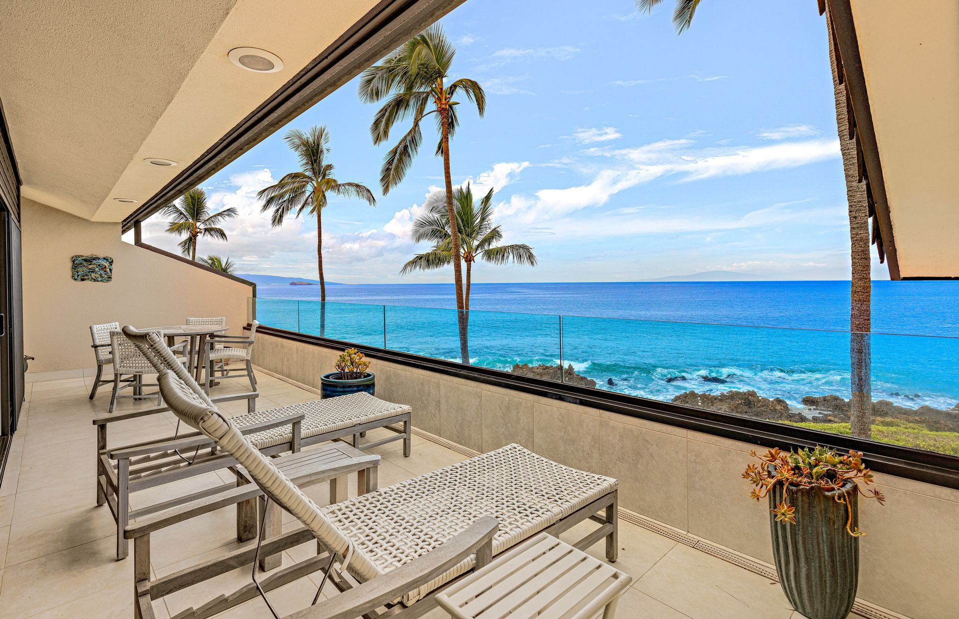 A balcony with a view of the ocean, equipped with wicker furniture and a potted plant.