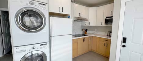 A compact kitchen with a built-in washer and dryer, a microwave, and wooden cabinets.