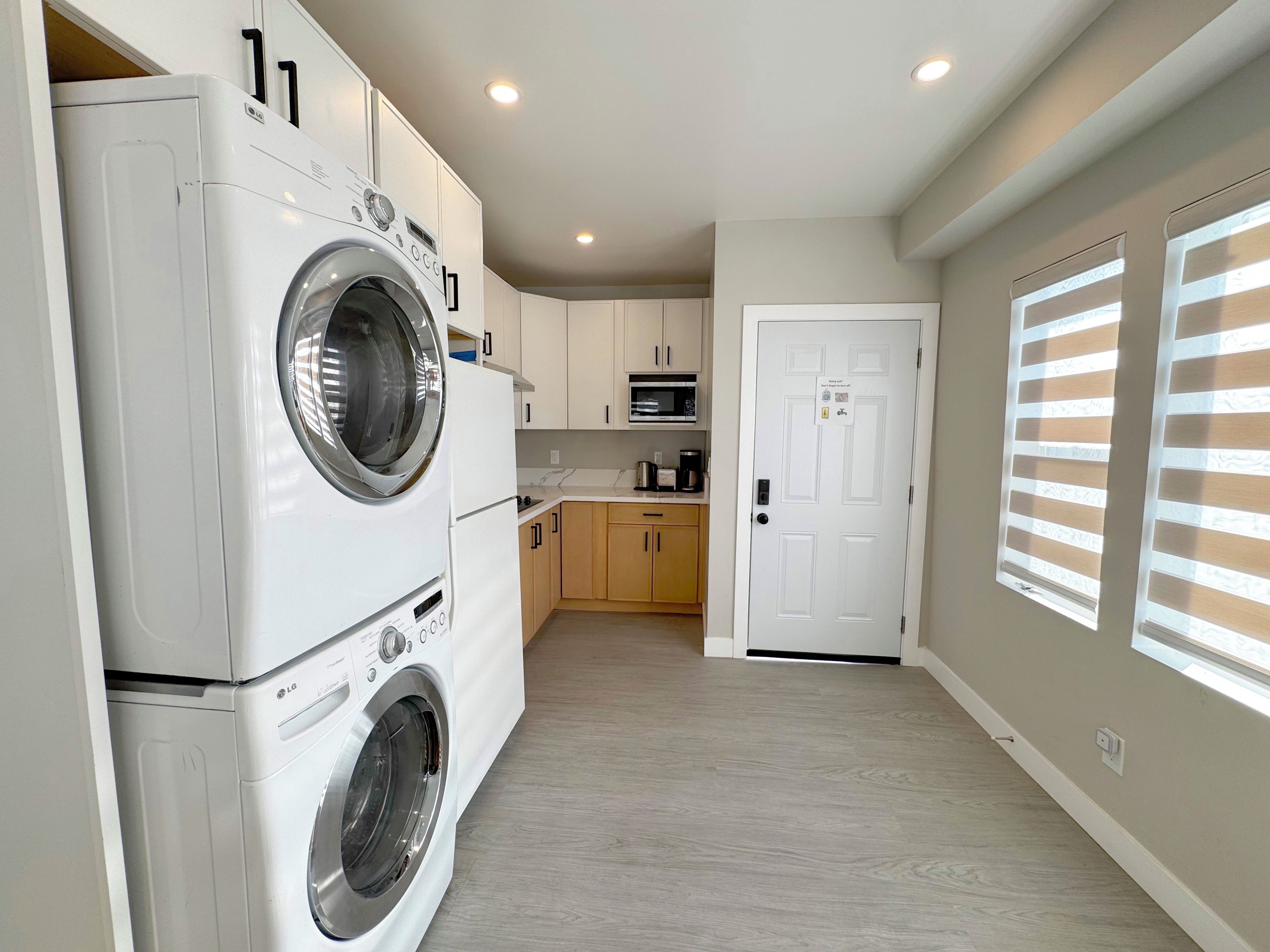 A laundry room with a front-loading washer and dryer, wooden cabinets, a microwave, and a door with a security lock.