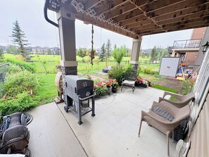 Une terrasse extérieure avec un barbecue, des meubles en osier et une vue sur un quartier résidentiel.