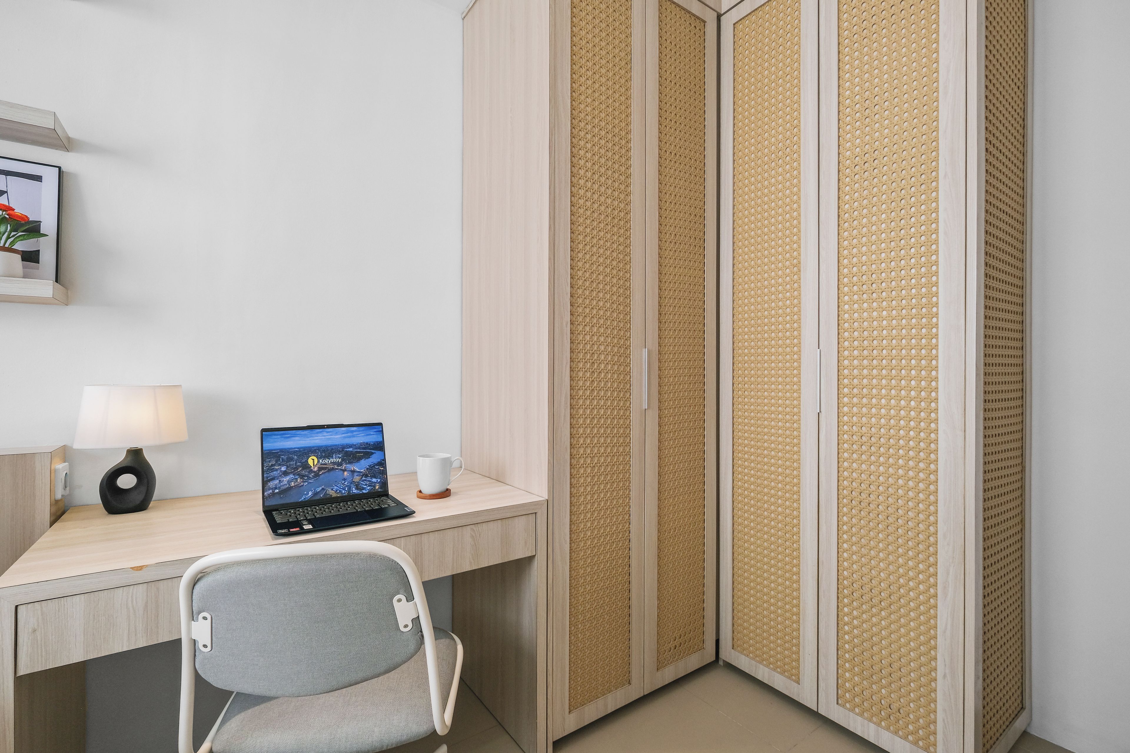A hotel room with a desk, laptop, lamp, and a view of a cityscape.