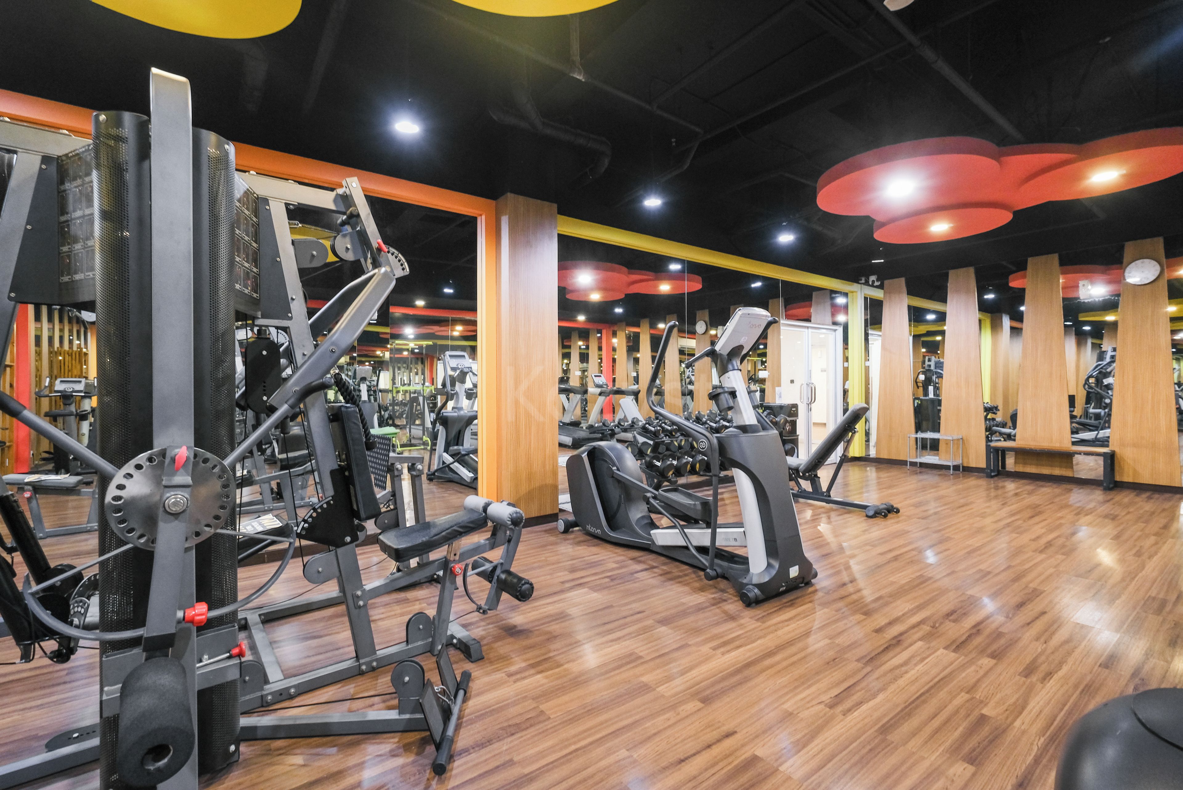 A gym with various exercise equipment, wooden flooring, and a modern design with yellow and red accents.