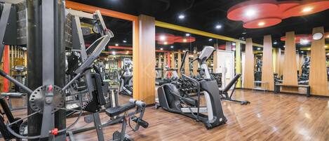 A gym with various exercise equipment, wooden flooring, and a modern design with yellow and red accents.
