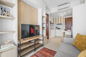 Ein modernes Wohnzimmer mit einem Flachbildfernseher, einer Couch, einem Couchtisch und einer Küche im Hintergrund.
