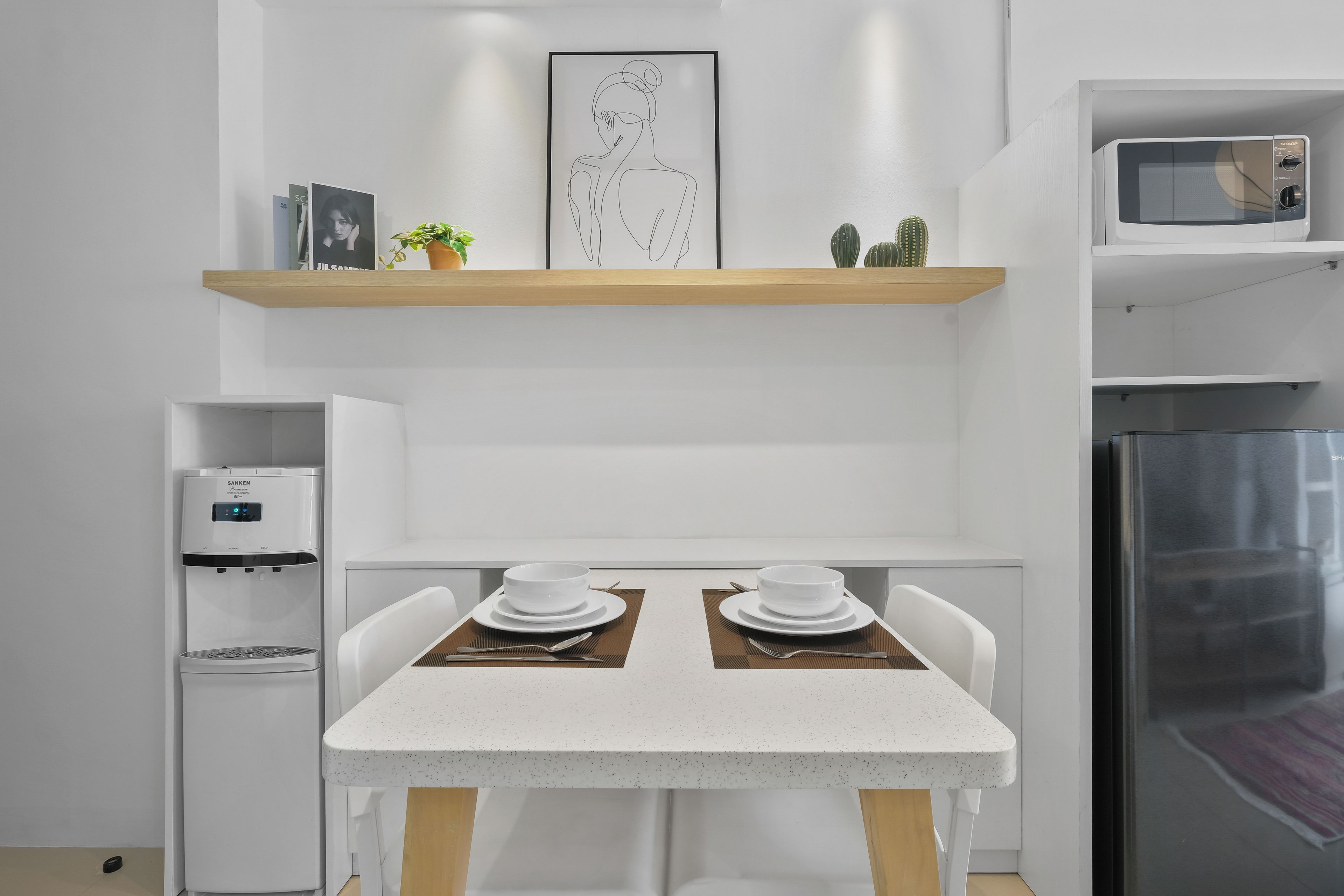 Eine moderne Küche mit weißer Arbeitsplatte, zwei weißen Stühlen, einem Edelstahl-Kühlschrank und einer Mikrowelle auf der rechten Seite.