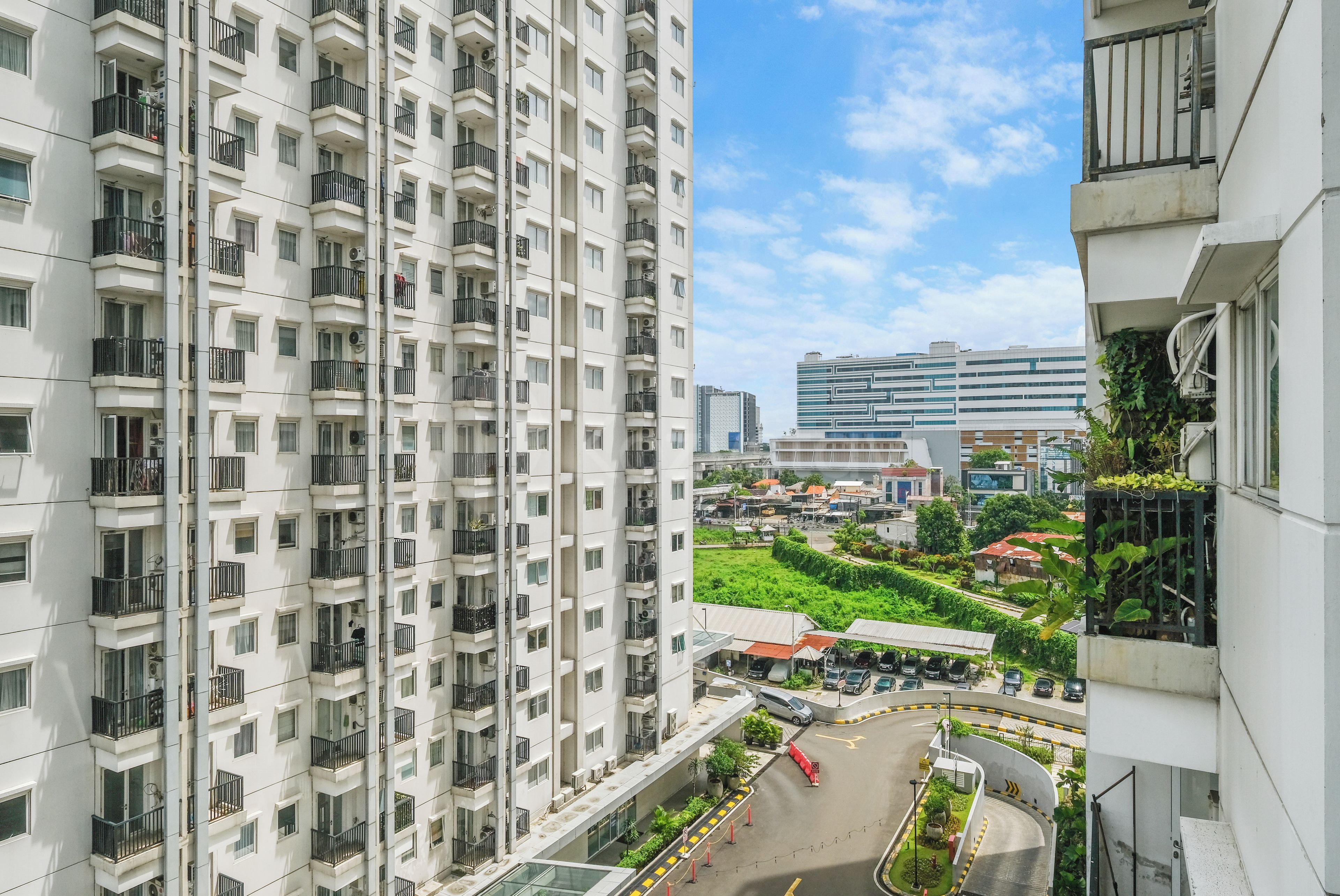 Un immeuble résidentiel de grande hauteur, doté de nombreux balcons, offrant une vue sur une route où circulent des voitures, et sur un bâtiment moderne situé au loin.