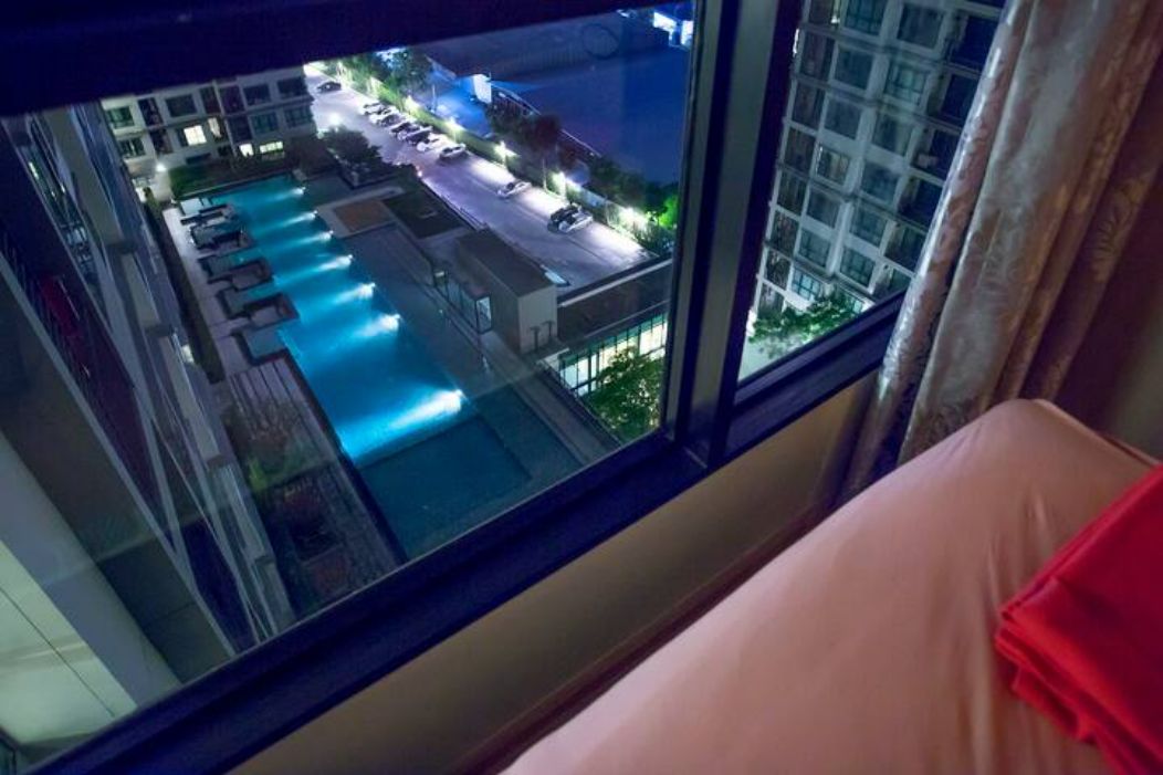 A room with a large window overlooking a swimming pool and a parking area.