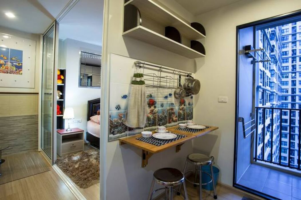 A compact kitchen with a built-in oven, a dining area with stools, and a view of a high-rise building through a large window.