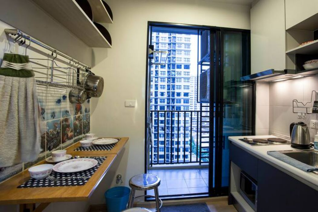 A compact kitchen with a dining area, a window with a view of a building, and a small stool.