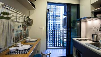 A compact kitchen with a dining area, a window with a view of a building, and a small stool.