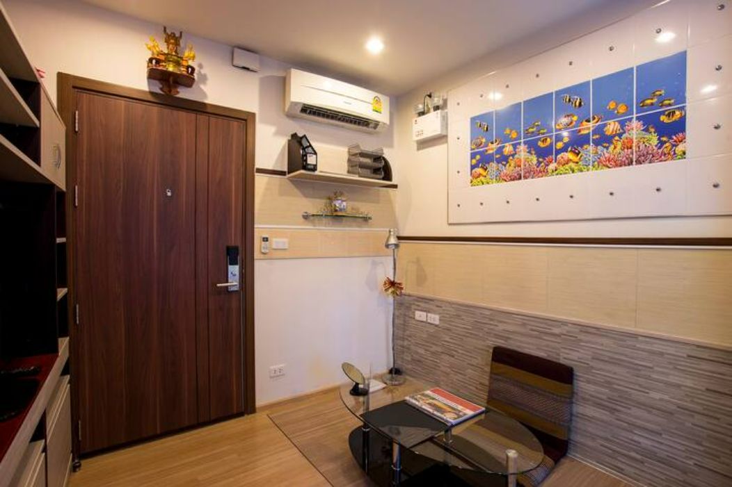 A hotel room with a wooden wardrobe, an air conditioning unit, a small table with a chair, and a wall with a marine life mural.