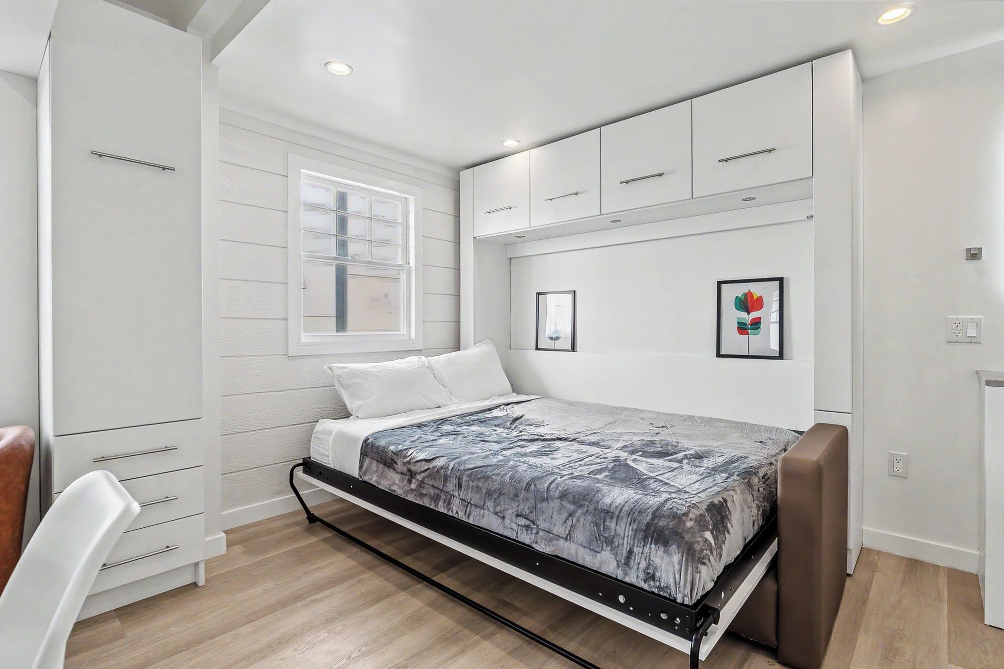 Quarto com cama, janela, guarda-roupa e prateleira fixada na parede.
