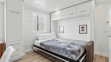 Quarto com cama, janela, guarda-roupa e prateleira fixada na parede.