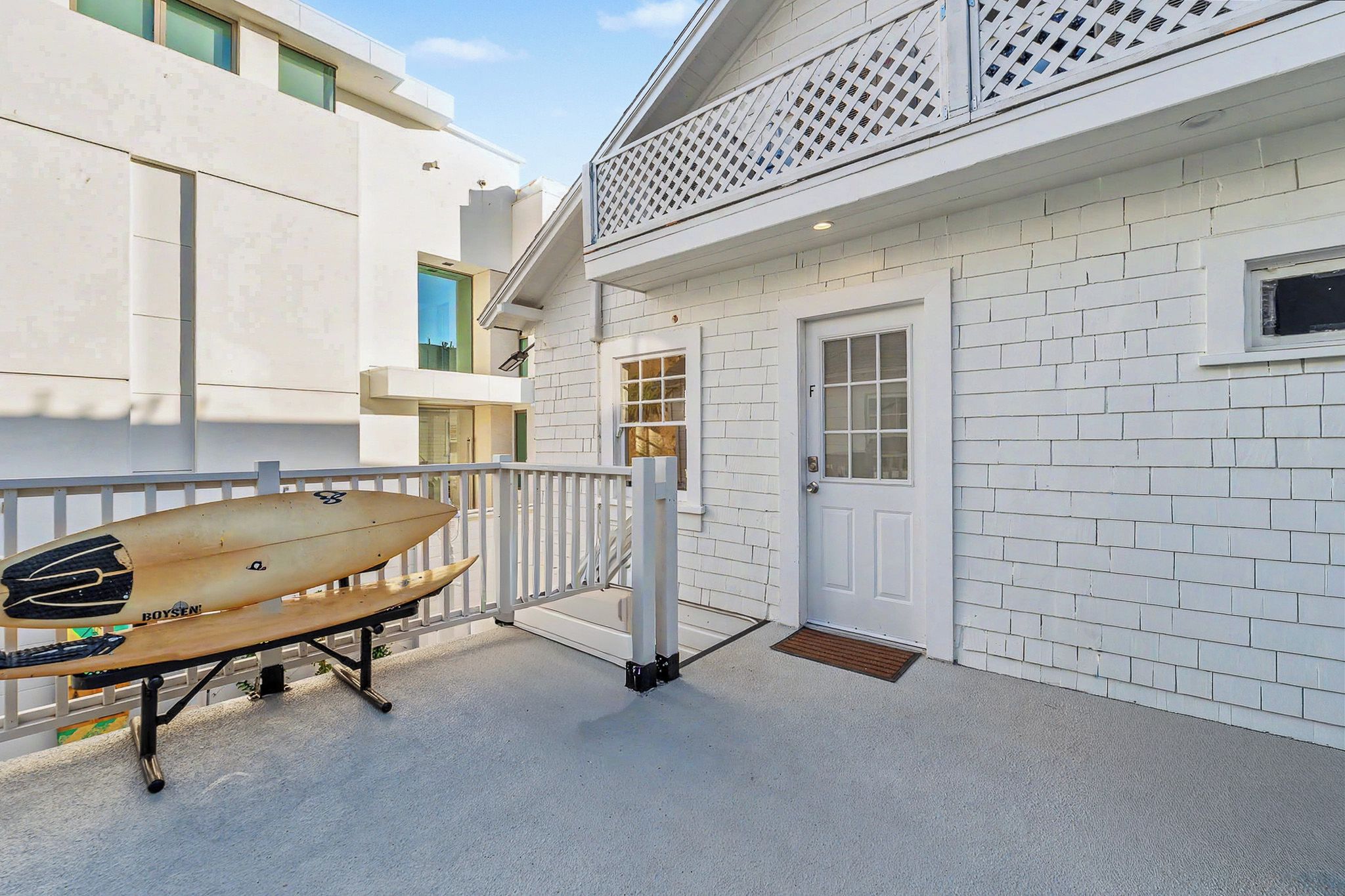 A white building with a door and window, a white fence, and a surfboard leaning against it.