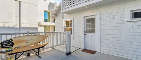 A white building with a door and window, a white fence, and a surfboard leaning against it.