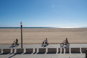 En strand med en asfalterad gångväg, en lyktstolpe och tre personer som cyklar.