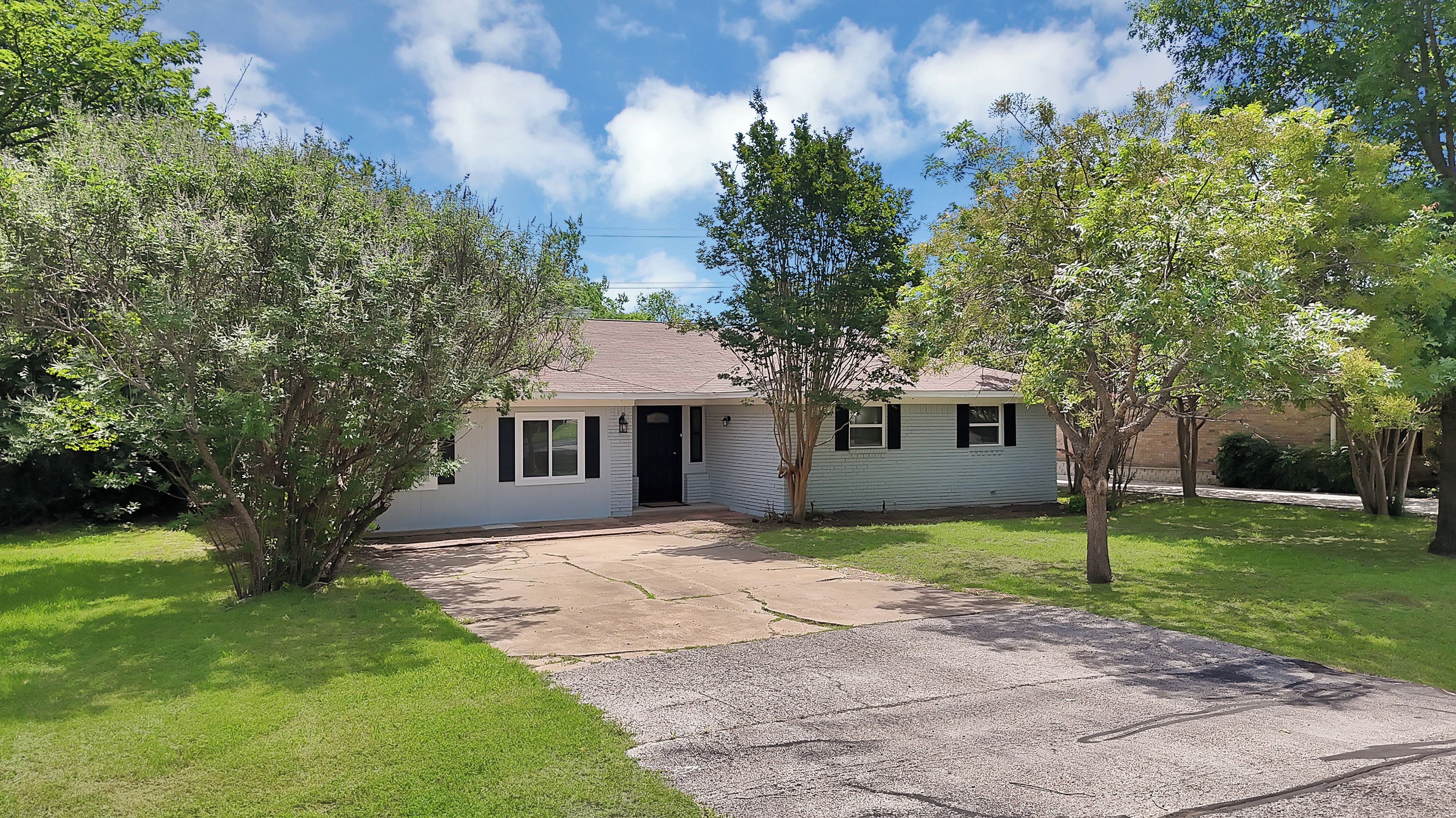 A single-story house with a front porch, surrounded by trees and a grassy yard.