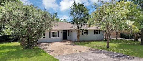 A single-story house with a front porch, surrounded by trees and a grassy yard.