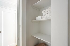 Ein weißer Kleiderschrank mit Regalen, eines davon ist mit gefalteten weißen Handtüchern bestückt.
