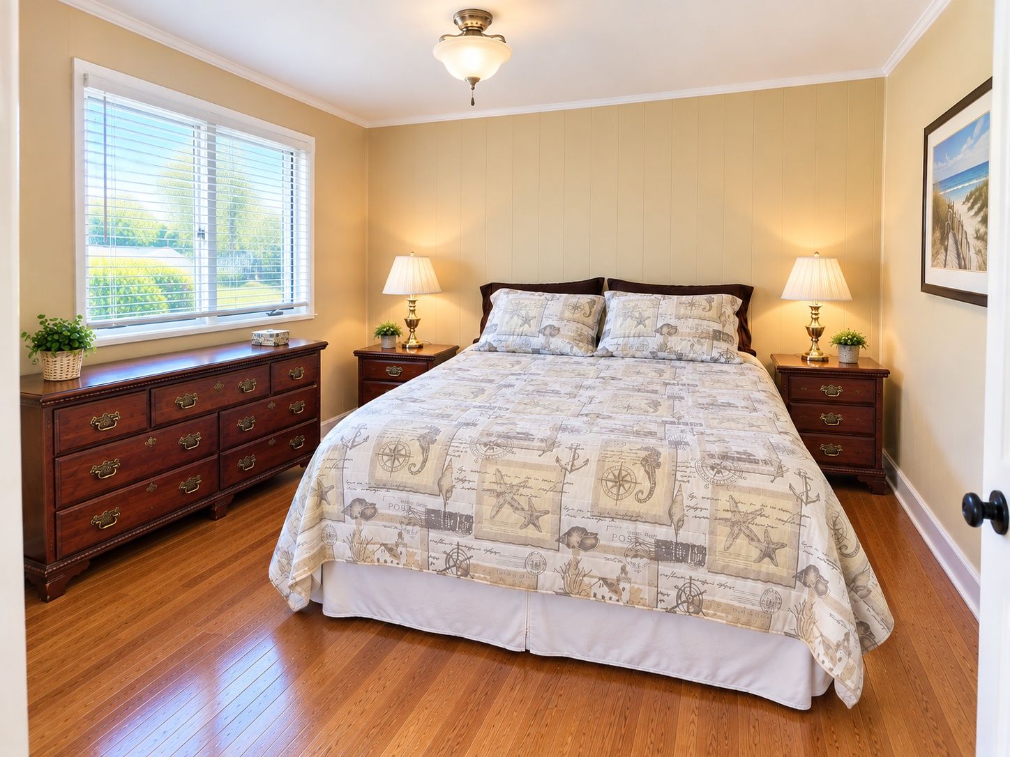 A bedroom with a large bed, two bedside tables with lamps, a dresser, and a window with blinds.