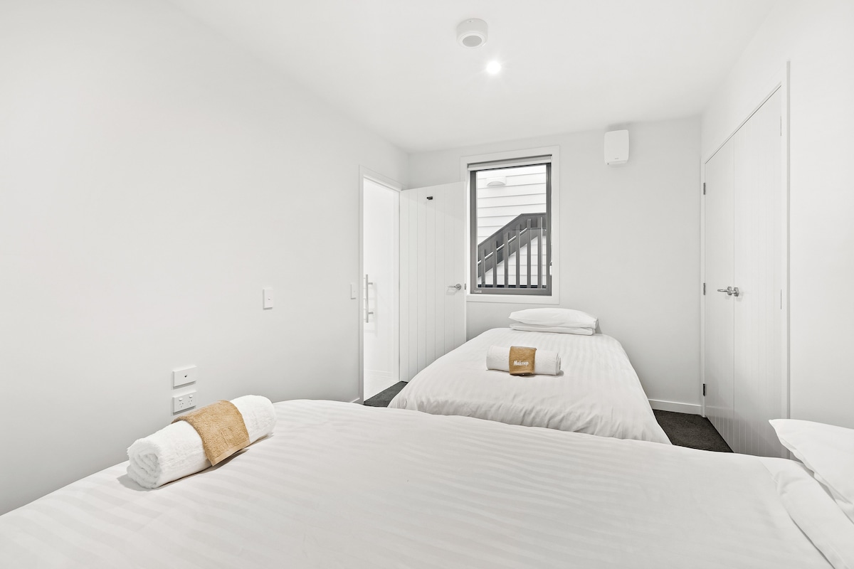 A hotel room with two beds, a window with a view of a staircase, and a door leading to another room.