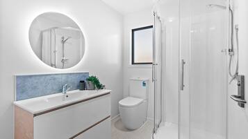 A modern bathroom with a round mirror, a white sink, a toilet, and a glass-enclosed shower area.