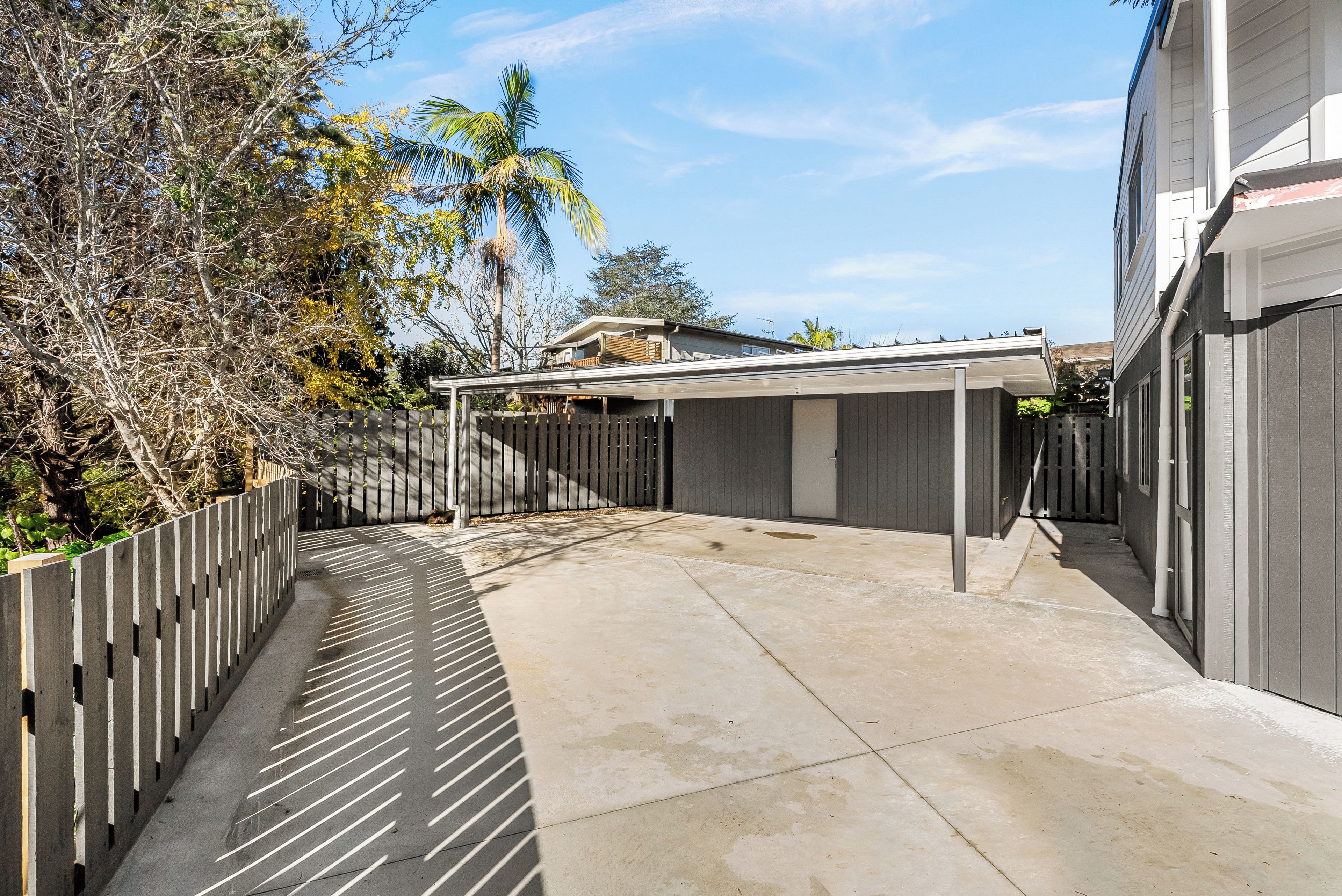 Un patio couvert avec un sol en béton, une clôture en bois et un bâtiment en arrière-plan.