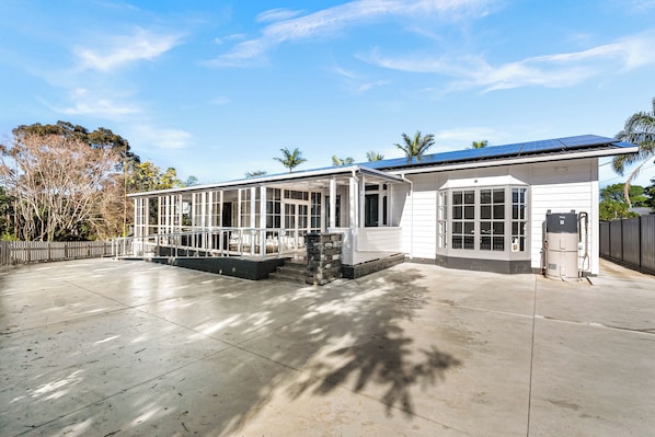 A two-story house with a covered patio, a stone fireplace, and a solar panel roof.