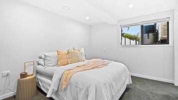 A bedroom with a bed, a bedside table, a lamp, a window, and a view of the outside.
