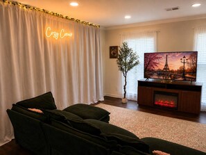 A living room with a sofa, a fireplace, a television, and a decorative plant. - Enchanted Forest | Hot Tub | Mins to ATL (Decatur)