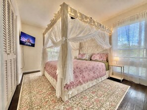 A bedroom with a four-poster canopy bed, a television mounted on the wall, and a window with blinds. - Enchanted Forest | Hot Tub | Mins to ATL (Decatur)