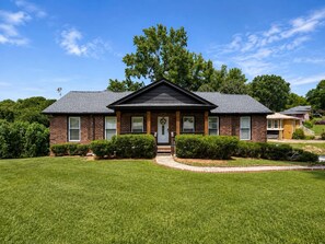 A two-story brick house with a front porch, a lawn, and a tree in the background. - Enchanted Forest | Hot Tub | Mins to ATL (Decatur)