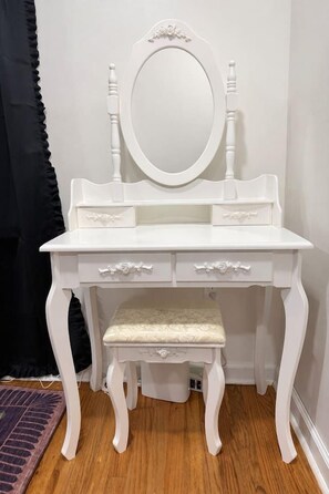 A white vanity with a mirror, two drawers, and a cushioned stool.