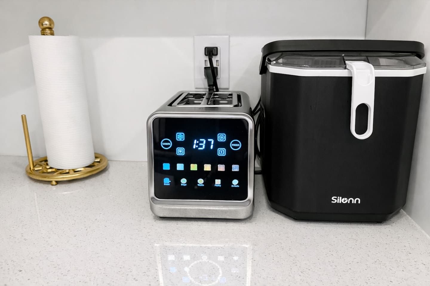 A modern kitchen with a digital toaster, a black coffee maker, and a roll of paper towels on a countertop.