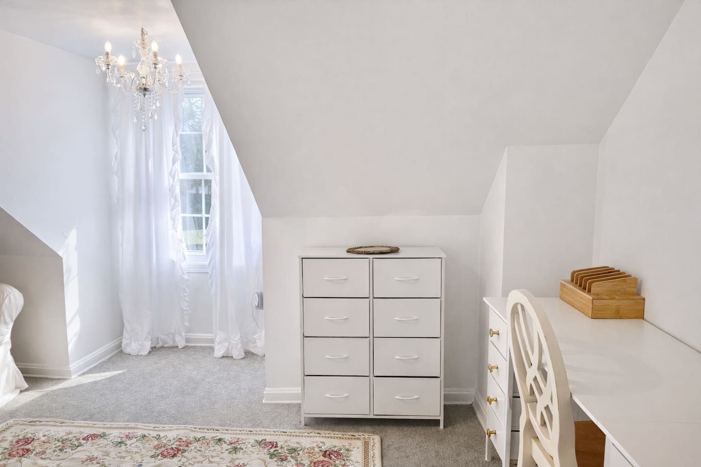 Een witte kamer met een kledingkast, een houten bijzettafeltje en een kroonluchter.