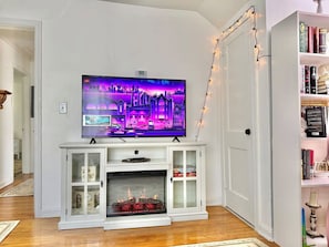 A living room with a flat-screen TV on a white entertainment unit, a fireplace, and a bookshelf. - Romantic Fairytale |10 min to Downtown (East Point)